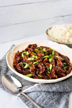 a white bowl filled with meat and vegetables next to rice on top of a table