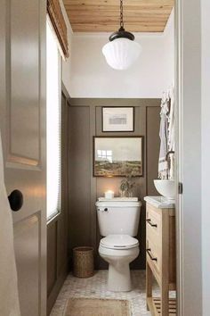 a white toilet sitting inside of a bathroom next to a wooden cabinet and sink under a light fixture