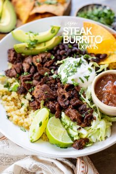 a white plate topped with meat, rice and beans next to guacamole