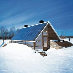 a small house with a solar panel on the roof in the middle of some snow