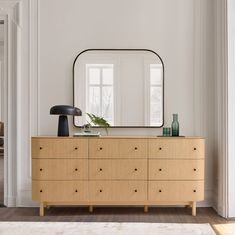 a dresser with a mirror and vases on it in front of a white wall