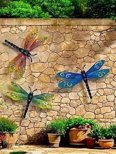 three colorful dragon sculptures on a stone wall in front of potted plants and flowers