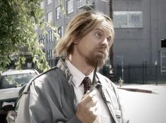 a man with long hair wearing a jacket and tie holding a pair of scissors in his hand