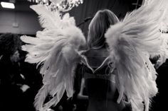 black and white photograph of woman with angel wings in front of chandelier hanging from ceiling