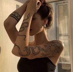 a woman with tattoos on her arms and arm is looking at the camera while standing in front of a window