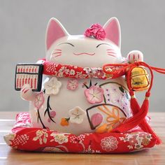 a white cat figurine sitting on top of a wooden table with a red ribbon around it's neck