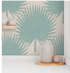 a white vase sitting on top of a counter next to a wall with palm leaves painted on it