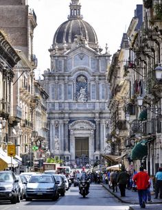 people are walking down the street in front of an old building with a dome on top