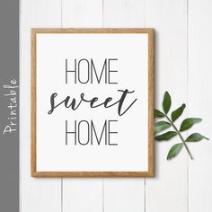 a sign that says home sweet home next to a plant on a white wooden surface