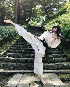 a woman is doing karate in front of some steps and trees on the other side