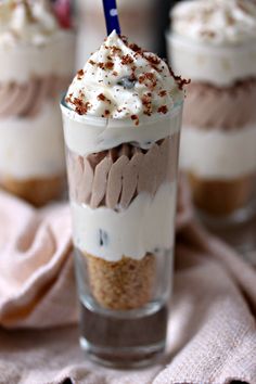 three desserts with whipped cream, chocolate and sprinkles in them on a pink cloth