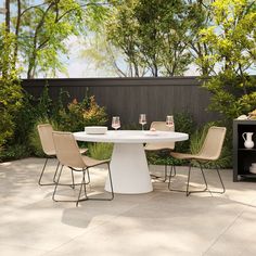 a white table with four chairs around it in the middle of a patio area surrounded by greenery