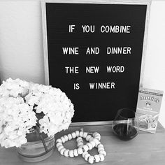 a black and white photo with some flowers on a table next to a sign that says if you combine wine and dinner the new word is winner