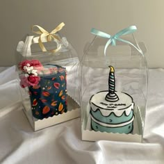 two birthday cakes sitting inside of clear boxes