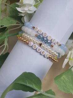 three beaded bracelets sitting on top of a white napkin next to some flowers