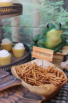 a table topped with cupcakes and cakes next to a frog figurine