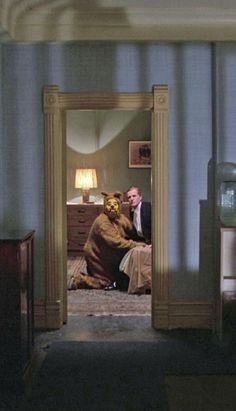 a man in a bear suit is sitting on the floor with his reflection in a mirror