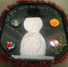 a snowman made out of buttons on a black tray with red tinsels