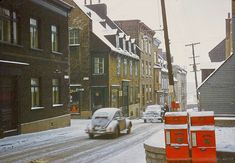 a car driving down a snow covered street next to tall brick buildings and traffic cones