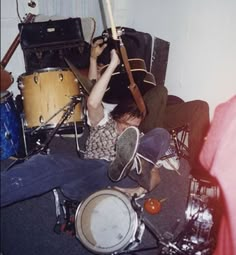 a man laying on the floor with his head in an open drum kit and other musical instruments behind him