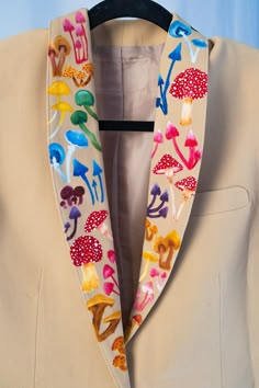 a tan jacket with colorful mushrooms on it and black hanger attached to the front