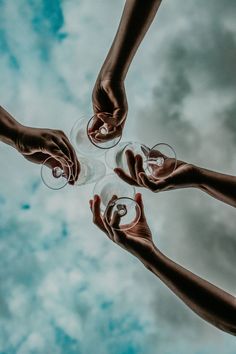 four hands holding wine glasses in the shape of a circle on a cloudy sky background