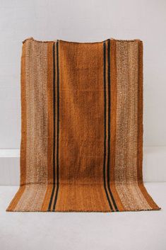 an orange and black striped rug sitting on top of a white floor next to a wall