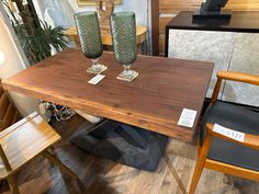 two green glass vases sitting on top of a wooden table next to a chair