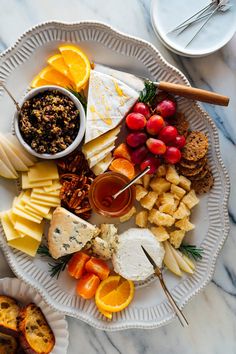 a white plate topped with cheese, fruit and crackers on top of a marble table