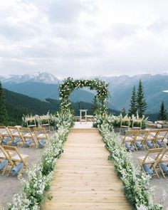 an outdoor ceremony setup with wooden chairs and greenery on the aisle, surrounded by mountains