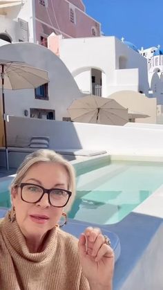 a woman wearing glasses sitting in front of an outdoor swimming pool