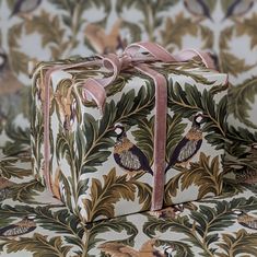 a gift box with a pink ribbon tied around it on top of a floral wallpaper