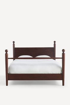 a wooden bed frame with white sheets and pillows