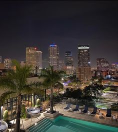 an outdoor swimming pool in front of a cityscape at night with palm trees and lounge chairs