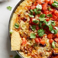 a pizza topped with tomatoes and cilantro on top of a pan filled with tortilla chips