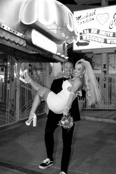 a bride and groom are posing for a photo in front of the neon sign at night