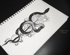 a spiral notebook with an image of two snakes and trees in the middle, on a black leather surface