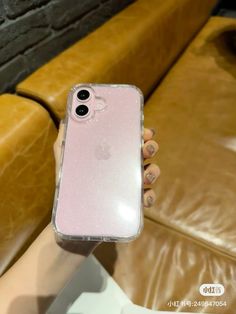 a person holding up a pink iphone case in front of a brown leather couch with a brick wall behind it