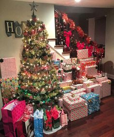 a christmas tree with presents under it in front of some stairs and other gifts on the floor