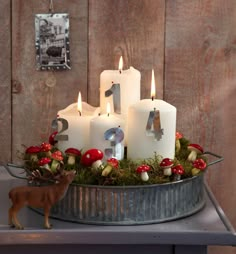 some candles are sitting in a tin with moss and mushrooms on it, next to a deer figurine