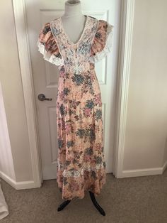 This nice vintage 70s peach burgundy green floral lace bib high waisted Maxi hippie dress comes to you in a size S. As you can see from pictures lace bodice over and then ties in back. Looks to be handmade cannot find a tag. Up material etc points to 70s dress.pls compare the measurements I give you to those in your closet. Overall great cond. 17 1/4 underarm to underarm -14/inches waist across- hips n/a-46 1/4 inches underarm to bottom of dress. Bohemian Floral Print Dress With Empire Waist, Bohemian Pink Lace Dress, Pink Bohemian Dress With Lace Patchwork, Hippie Fitted Dress With Ruffles, Cottagecore V-neck Dress With Lace Trim, Fitted Hippie Pink Dress, Fitted Pink Hippie Dress, Pink Bohemian Dress With Lace Trim, Bohemian Lined Dress For Garden Party