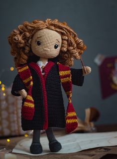 a crocheted doll dressed in a harry potter outfit holding a wand and wearing a scarf