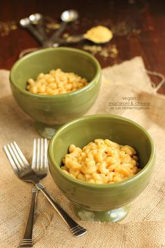 two green bowls filled with macaroni and cheese on top of a table next to silverware