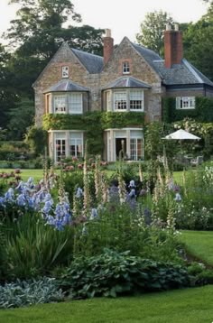 a large house surrounded by lots of flowers and greenery in front of the house