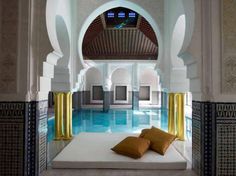 an indoor swimming pool surrounded by arches and columns with pillows on the bed in front