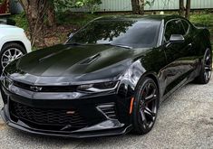 the black chevrolet camaro is parked in front of two other white and gray cars