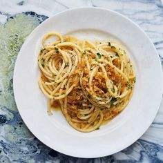 a white plate topped with pasta covered in sauce and parmesan cheese on top of a marble table