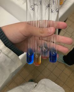 a person holding four test tubes filled with blue liquid and yellow liquids in their hands