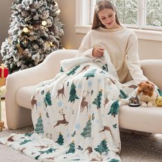 a woman sitting on a couch under a blanket next to a cat and christmas tree