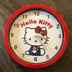 a hello kitty clock on a wooden table with the words hello kitty painted on it